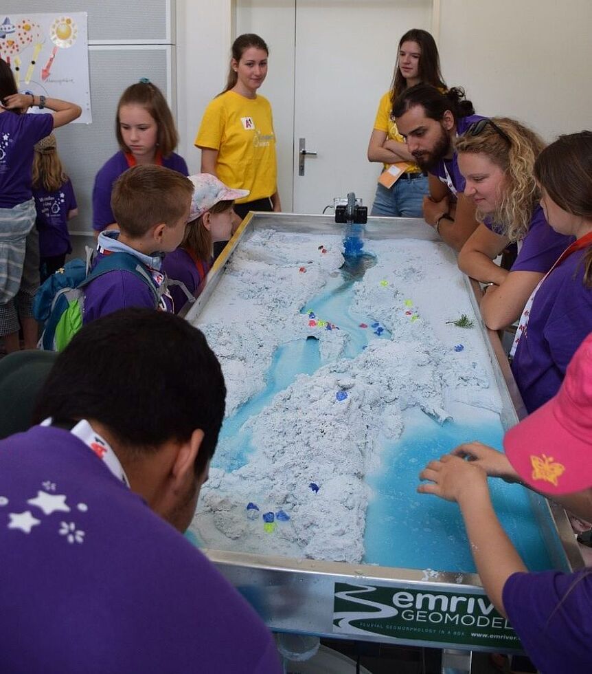 Kinder und Workshopleiter beobachten die Dynamik des Abflusses an einem Flussmodells
