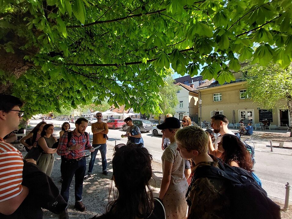 Domen Žalac pointing out post-modern houses along a touristified street next to Gradaščica river. A socialist block is visible behind. (©Thurner, 2023)