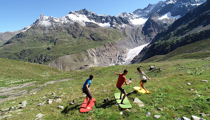 Studierende "surfen" auf Unterlegsmatten eine Almwiese hinunter (C) Ulrich Zangerl - Freude im Feld
